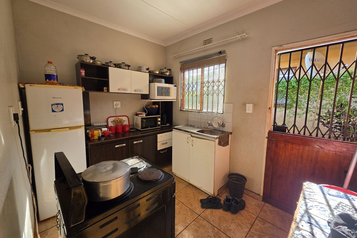 A functional kitchen featuring built-in cabinetry, a stainless steel sink, and tiled flooring, with direct access to the exterior via a security gate.