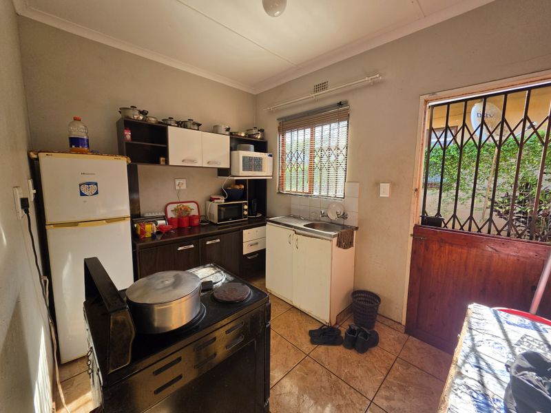 A functional kitchen featuring built-in cabinetry, a stainless steel sink, and tiled flooring, with direct access to the exterior via a security gate.