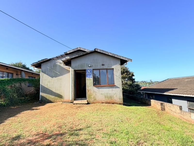 Rear view of a detached house featuring a tiled roof, aluminium window frames, and a surrounding lawn area with boundary walling.