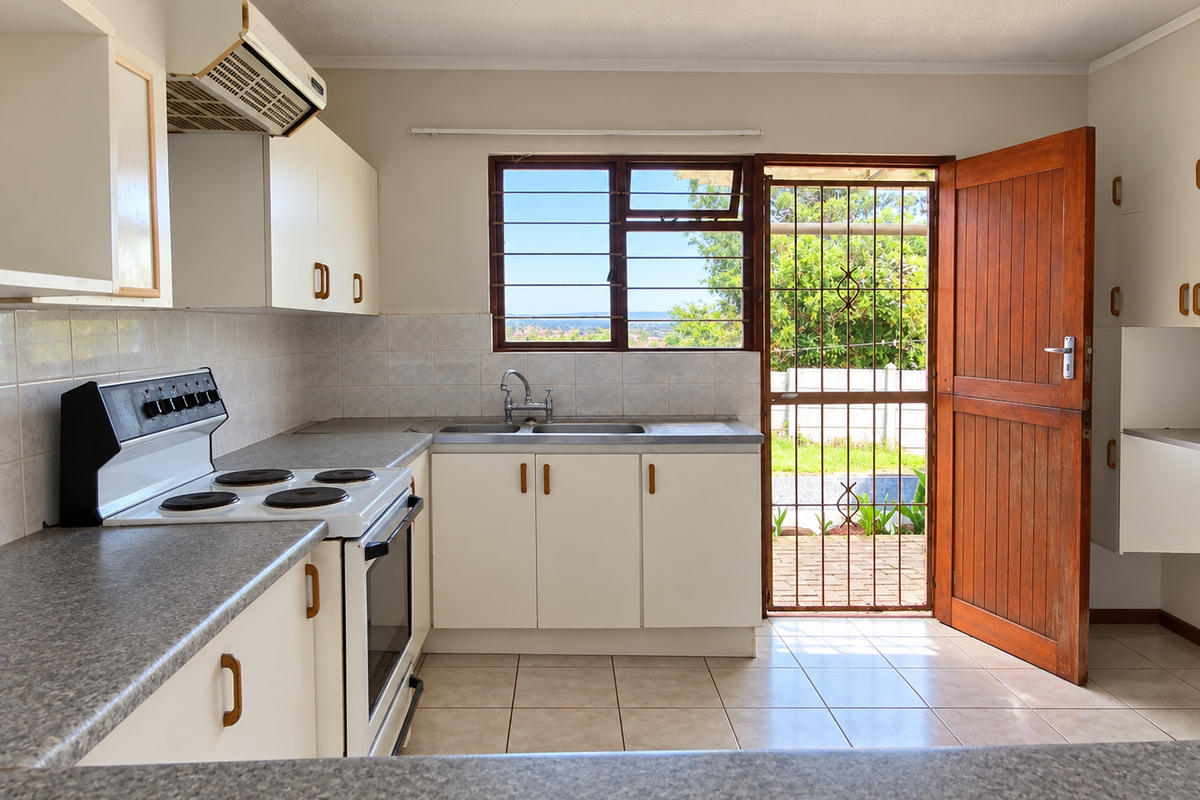 A functional kitchen featuring built-in cabinetry, laminate countertops, and an electric stove, with direct access to the rear garden through a timber door.