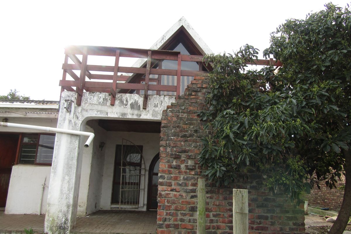 Rear exterior view of the property featuring a paved patio, exposed brick wall, and an upper-level wooden balcony.