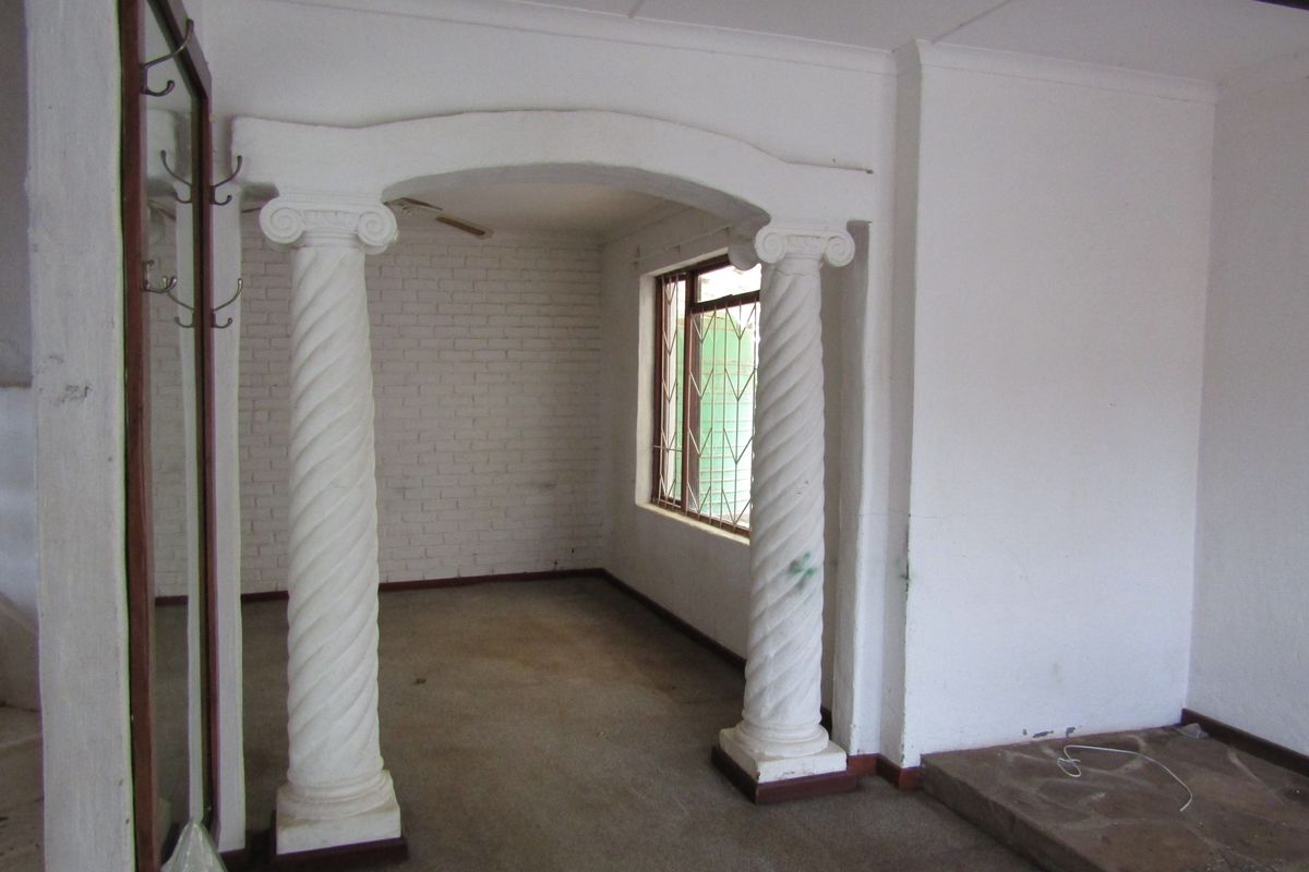 An empty living area featuring decorative spiral columns, an arched entryway, exposed brick wall detailing, and a stone hearth.