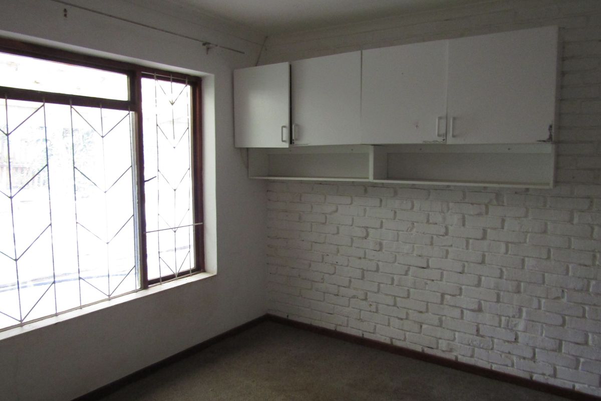 An empty bedroom featuring a painted brick wall, built-in overhead storage cabinets, and security bars on the window.
