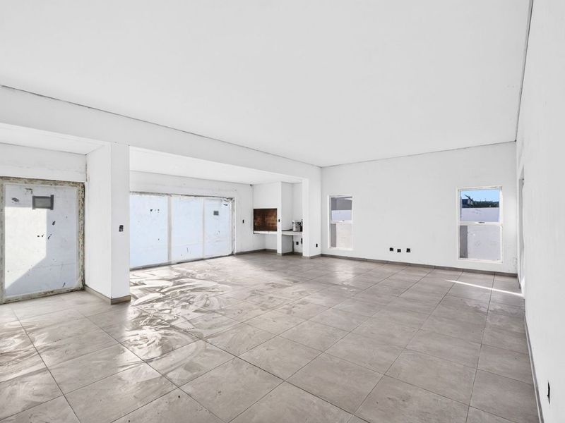 Spacious open-plan living area featuring large format floor tiles, built-in braai, and expansive sliding doors leading to the exterior.