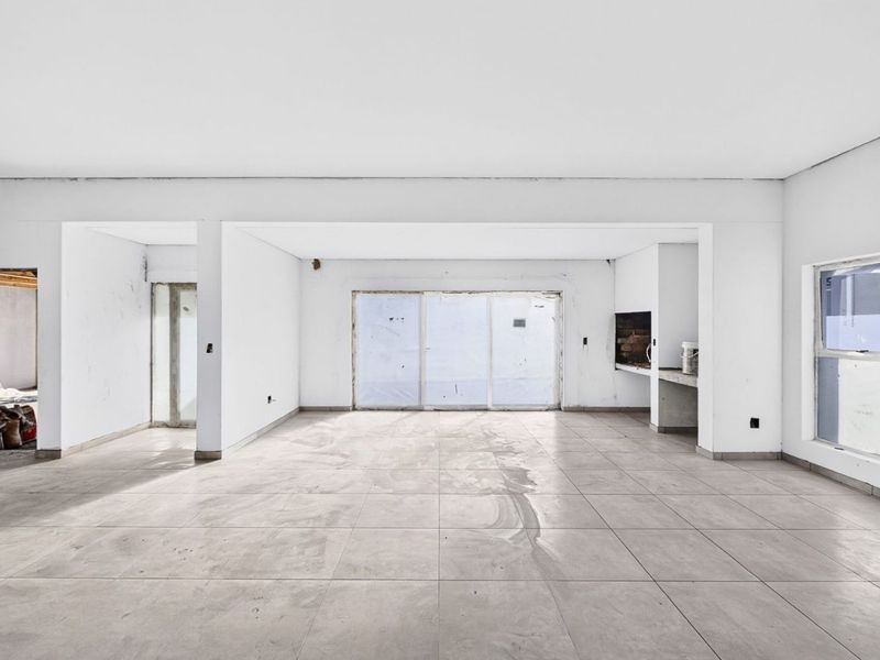 Spacious open-plan living area featuring large format floor tiles, a built-in braai, and sliding doors leading to the exterior.