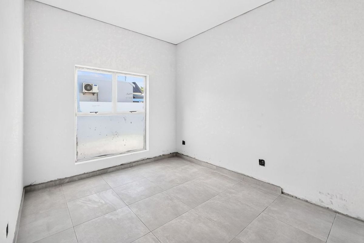 An empty, neutral-toned bedroom featuring tiled flooring and a large window, awaiting final finishes and personal touches.