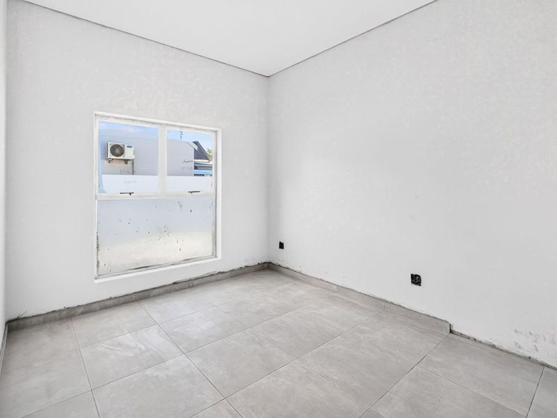 An empty, neutral-toned bedroom featuring tiled flooring and a large window, awaiting final finishes and personal touches.