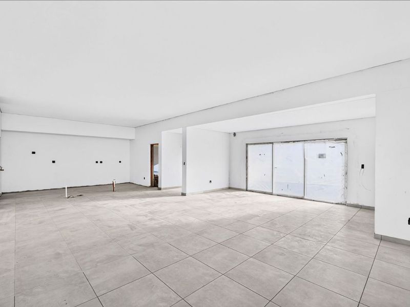 A spacious, open-plan living area featuring large format floor tiles and sliding glass doors, currently in an unfinished state awaiting final interior finishes.