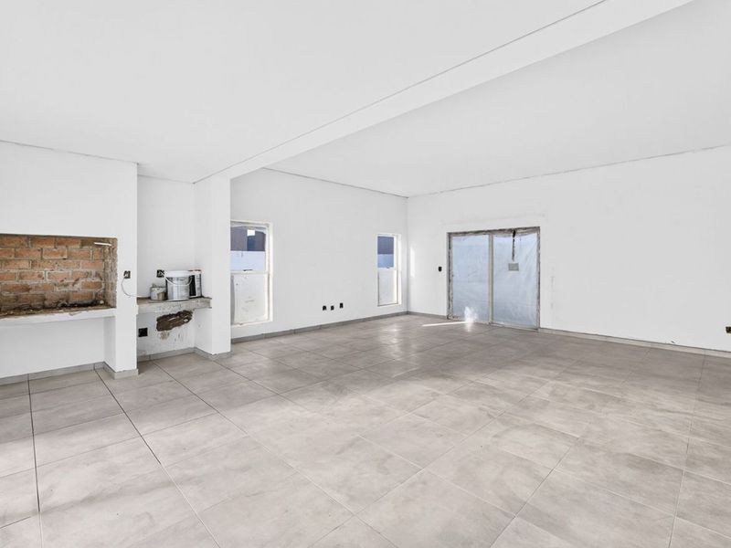 Spacious open-plan living area featuring large format floor tiles, an unfinished built-in fireplace, and sliding door access to the exterior.
