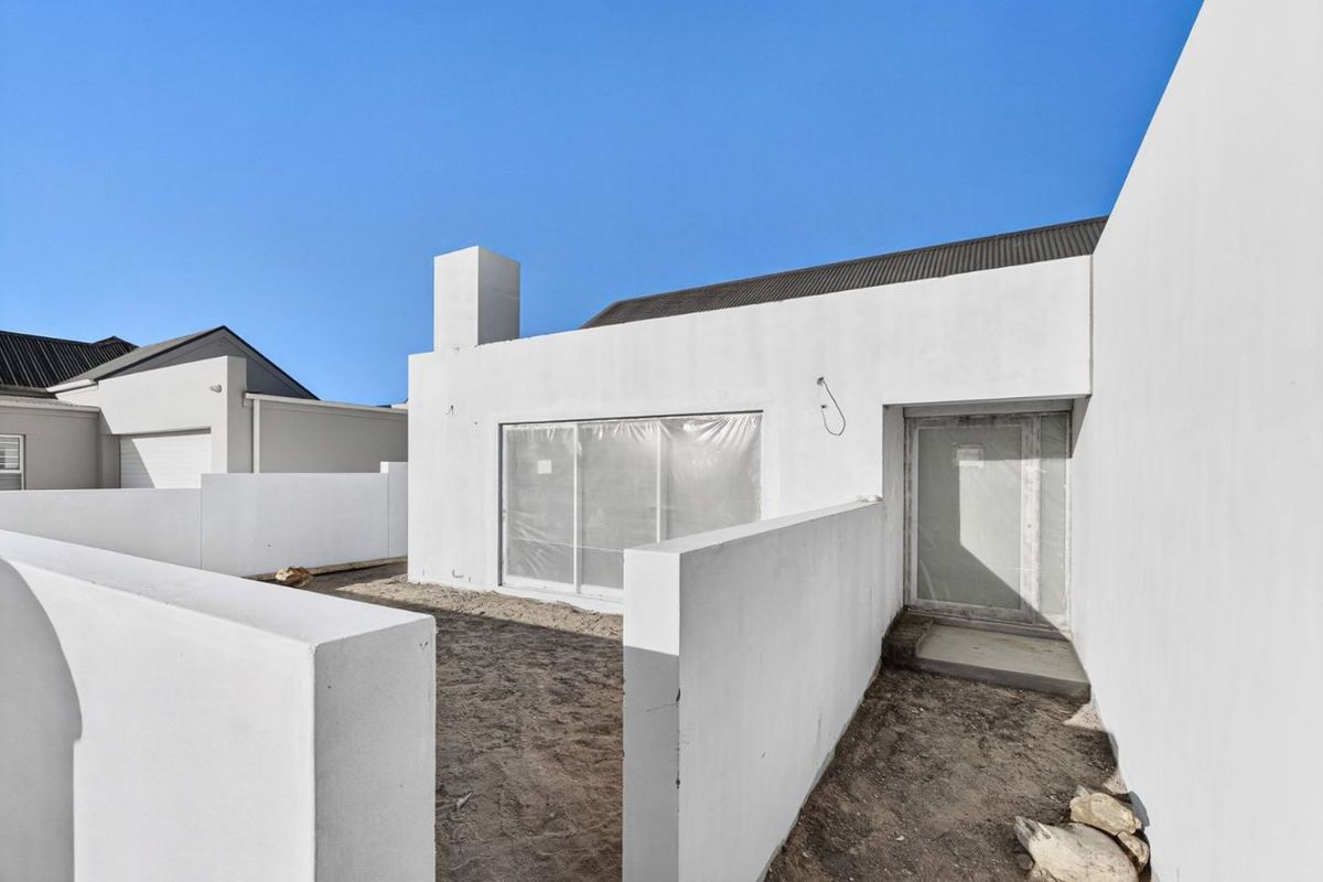 Rear exterior view of a modern house featuring a chimney, sliding glass door, and boundary walls, currently in the final stages of construction.