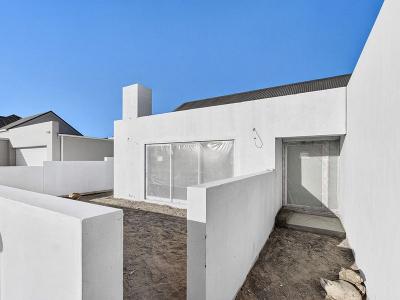 Rear exterior view of a modern house featuring a chimney, sliding glass door, and boundary walls, currently in the final stages of construction.
