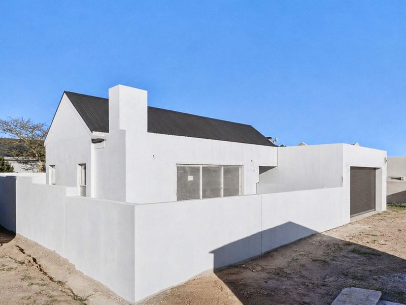 A modern white exterior facade featuring a dark corrugated metal roof, integrated garage, and surrounding boundary wall, set on an undeveloped plot.