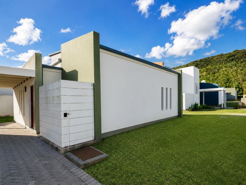 Rear exterior view of the townhouse featuring a paved driveway, covered patio area, and a well-maintained lawn with modern architectural wall detailing.