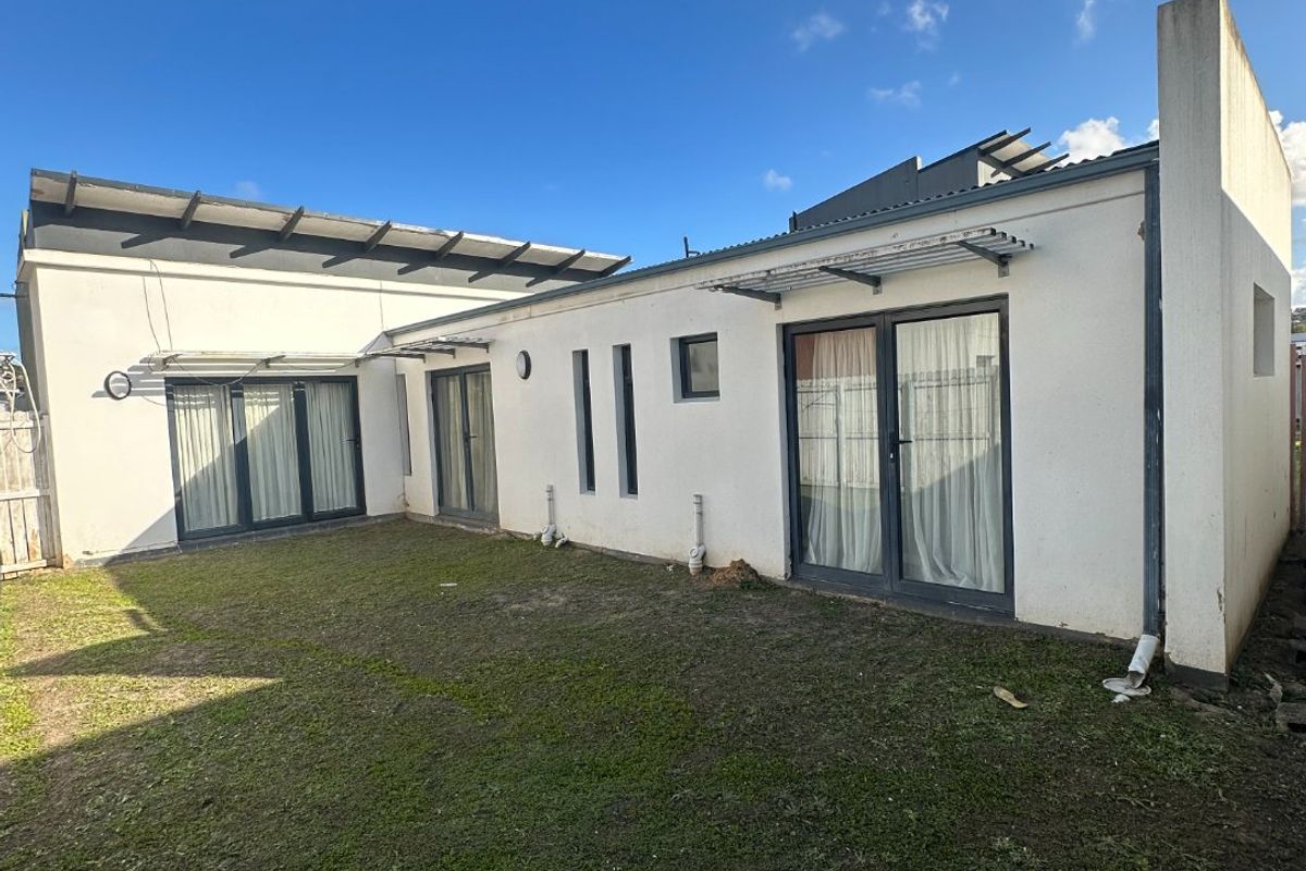 Rear view of the townhouse featuring a private lawn area, multiple sliding glass doors, and modern metal awnings.