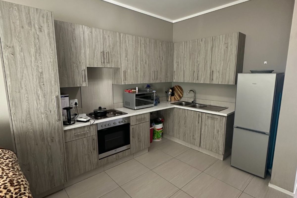 A functional kitchen featuring modern wood-look cabinetry, tiled flooring, integrated oven and hob, and ample counter space for meal preparation.