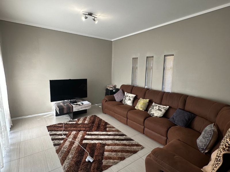 A well-maintained living room featuring neutral tiled flooring, modern ceiling spotlights, and unique vertical slit windows, providing a clean and functional space.