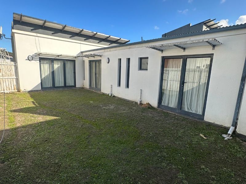 Rear view of the townhouse featuring a private garden area with sliding glass doors and metal roof awnings.