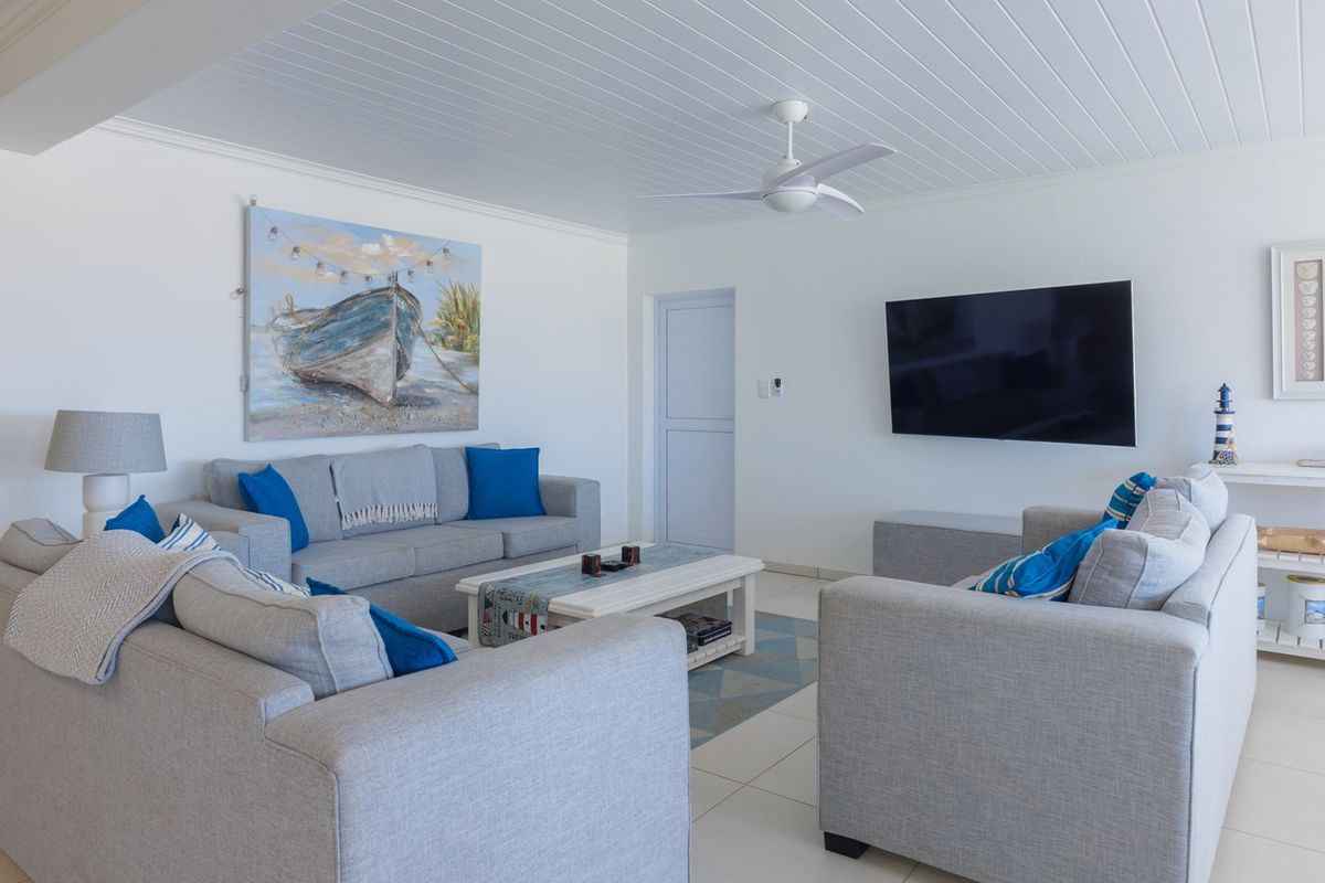 A bright and well-maintained living room featuring a white tongue and groove ceiling, a modern ceiling fan, and neutral tiled flooring.
