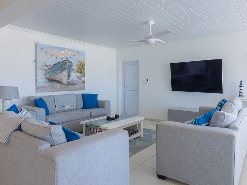 A bright and well-maintained living room featuring a white tongue and groove ceiling, a modern ceiling fan, and neutral tiled flooring.