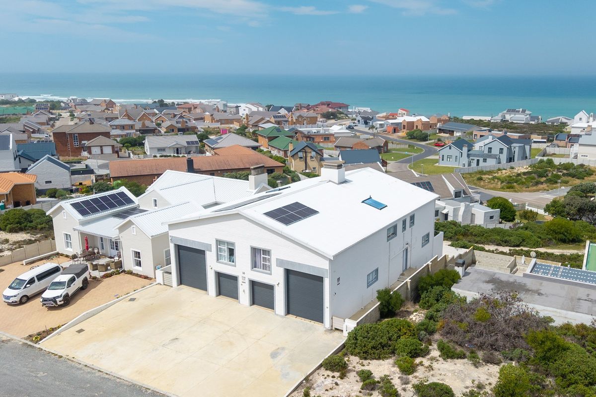 Aerial view of a coastal property featuring a multi-car garage, solar panels, and a metal roof, situated in a residential neighborhood near the ocean.