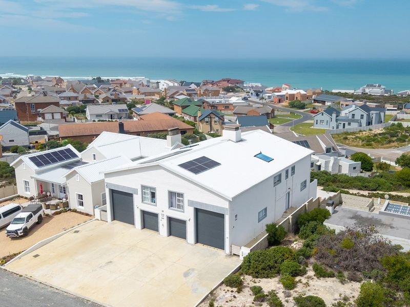 Aerial view of a coastal property featuring a multi-car garage, solar panels, and a metal roof, situated in a residential neighborhood near the ocean.