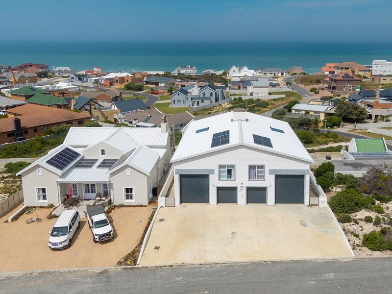 Aerial view of a coastal property featuring a main residence and a large detached garage building with solar panels and paved driveway.