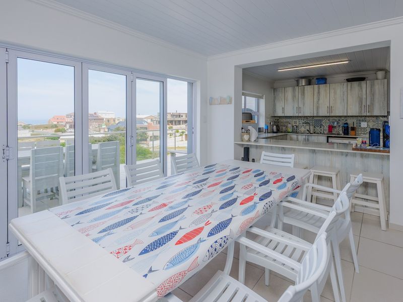 Open-plan kitchen and dining area featuring tiled floors, built-in cabinetry, and large sliding doors leading to an outdoor patio with coastal views.