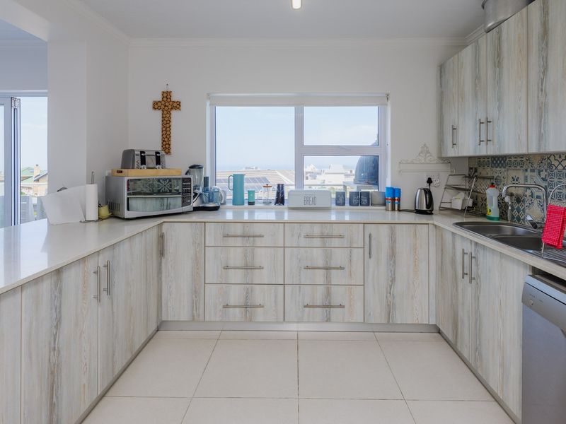 A functional kitchen featuring light wood-grain cabinetry, stone countertops, a decorative tiled backsplash, and a bright window overlooking the exterior.