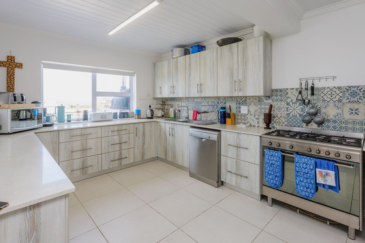 A functional kitchen featuring light wood-grain cabinetry, a gas stove with oven, patterned tiled backsplash, and neutral floor tiles.