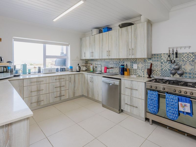 A functional kitchen featuring light wood-grain cabinetry, a gas stove with oven, patterned tiled backsplash, and neutral floor tiles.