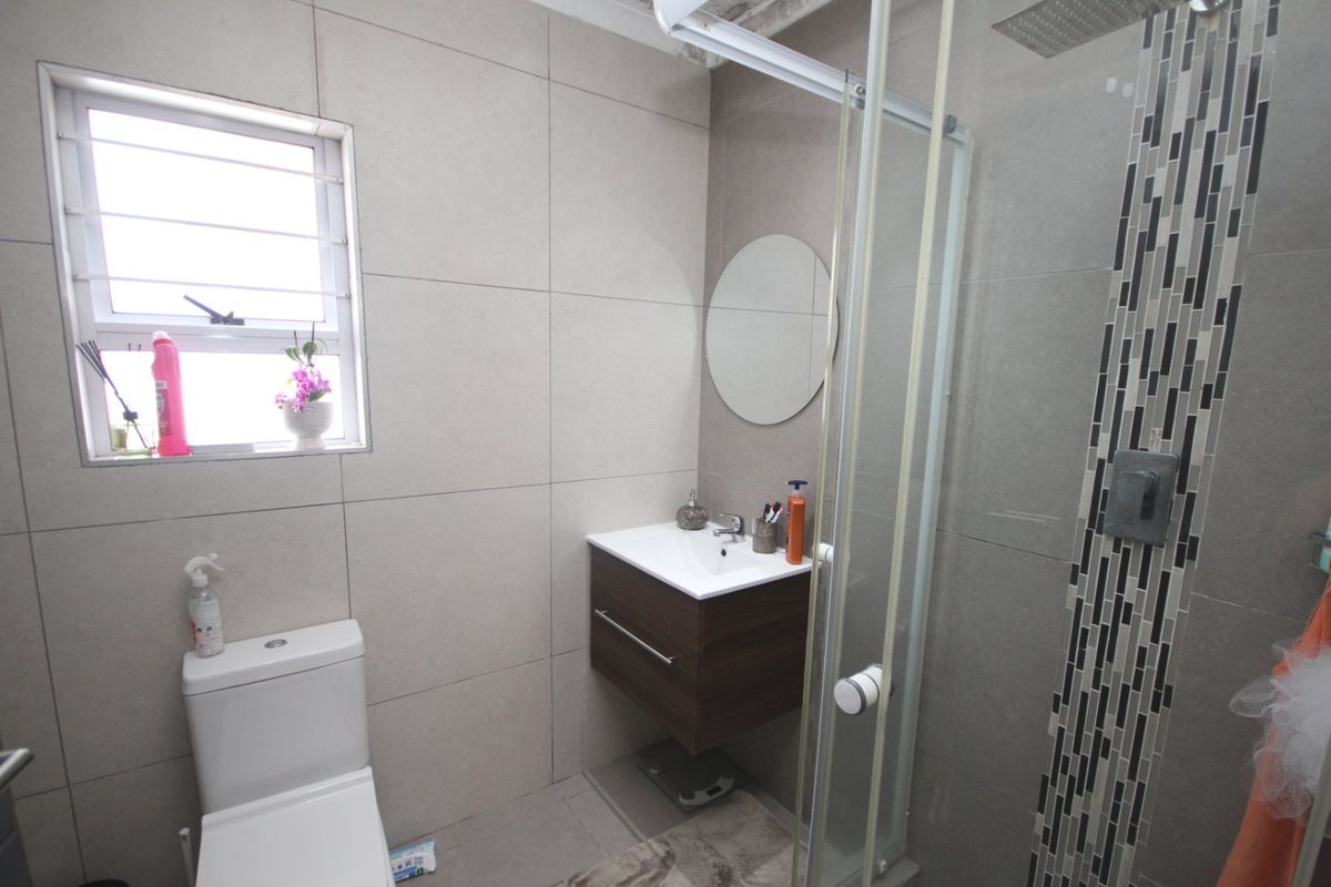 A modern bathroom featuring a wall-mounted vanity, a glass-enclosed shower with decorative mosaic tile accents, and neutral wall tiling.