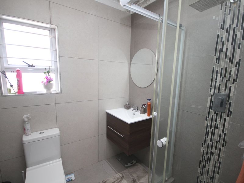 A modern bathroom featuring a wall-mounted vanity, a glass-enclosed shower with decorative mosaic tile accents, and neutral wall tiling.