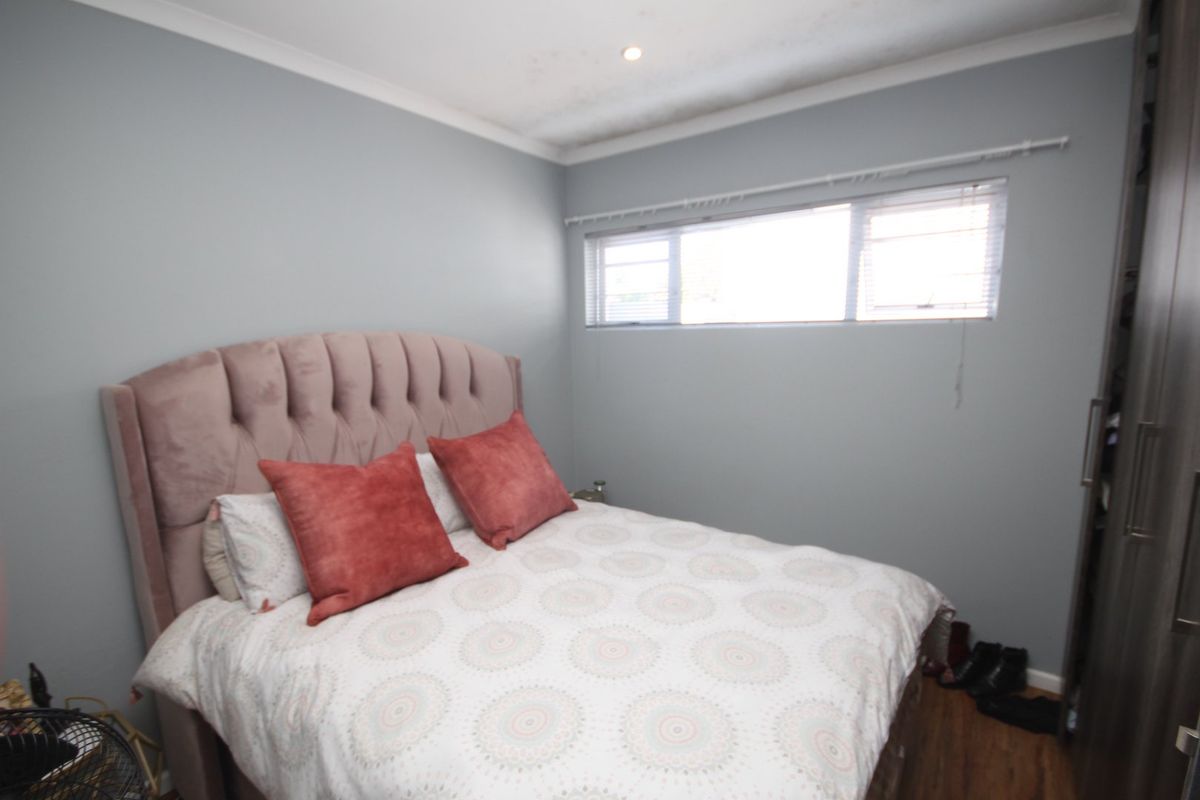 A bedroom featuring laminate flooring, built-in wardrobes, and recessed downlighting. The room includes a window with fitted blinds.