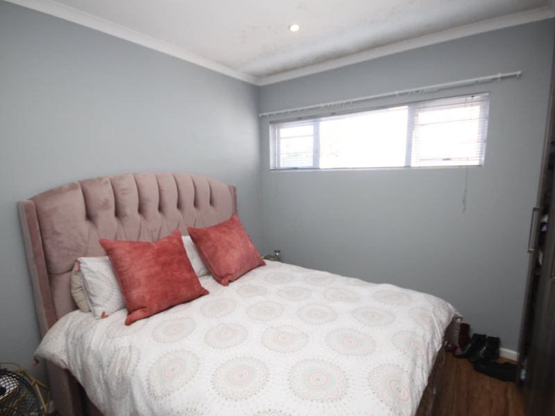 A bedroom featuring laminate flooring, built-in wardrobes, and recessed downlighting. The room includes a window with fitted blinds.