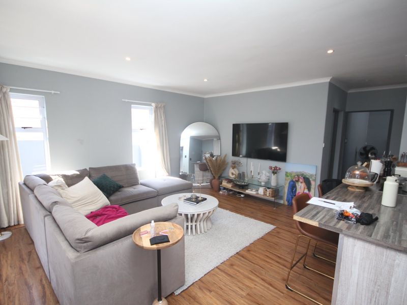 An open-plan living area featuring laminate flooring, recessed downlights, and a kitchen breakfast bar, creating a functional and connected living space.