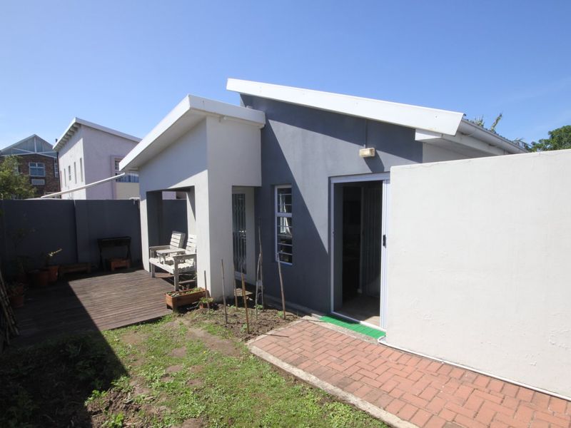 Rear view of the townhouse featuring a timber deck, paved walkway, and a small garden area with boundary walls.