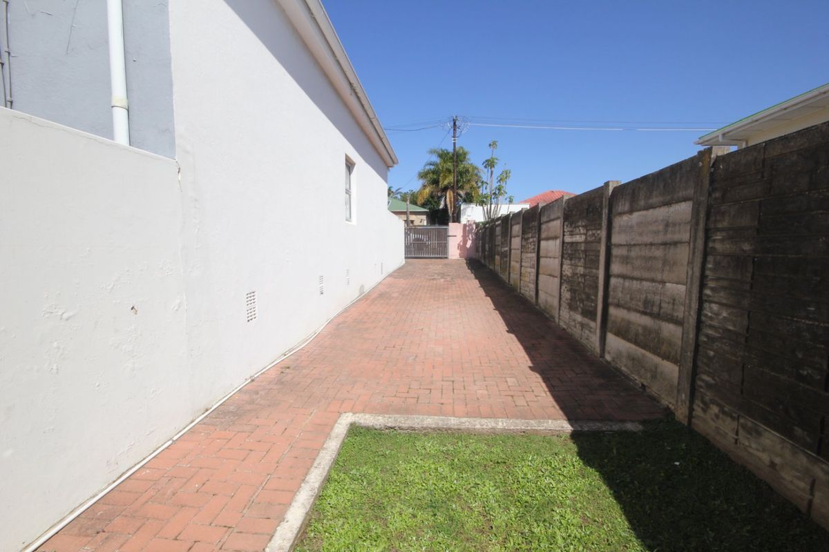 A side exterior view of the townhouse featuring a paved walkway, a small lawn area, and a precast concrete boundary wall.