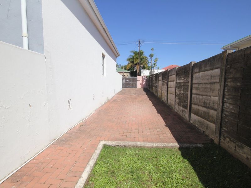 A side exterior view of the townhouse featuring a paved walkway, a small lawn area, and a precast concrete boundary wall.