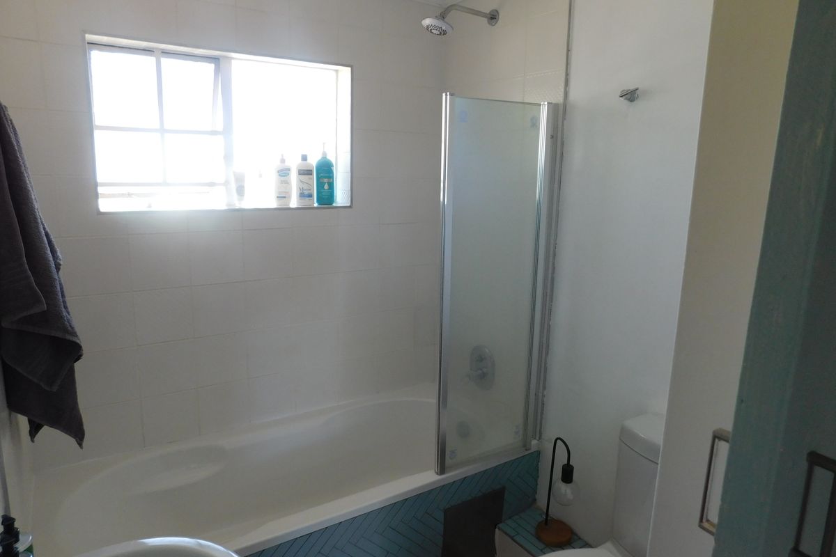 A functional bathroom featuring a bathtub with an integrated shower, glass screen, and decorative herringbone tiling on the bath apron.