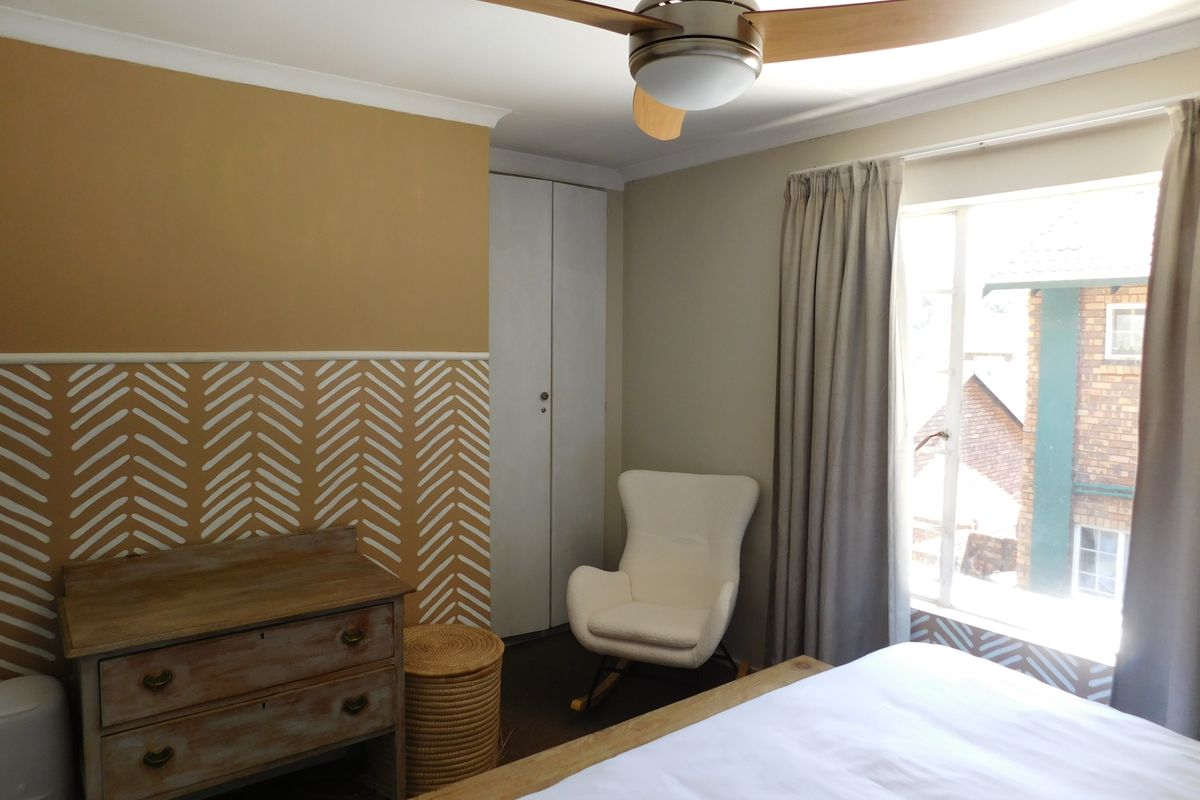 A bedroom featuring a built-in wardrobe, ceiling fan, and decorative wall treatment, offering a functional space with natural light.