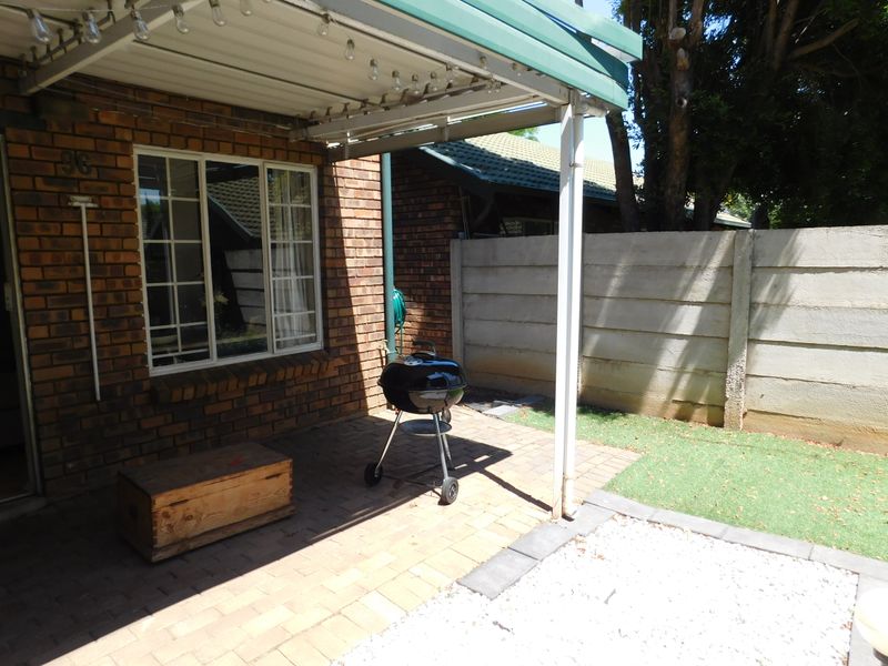 A private covered patio area featuring brick exterior walls, paved flooring, and a small adjacent garden space with a precast boundary wall.