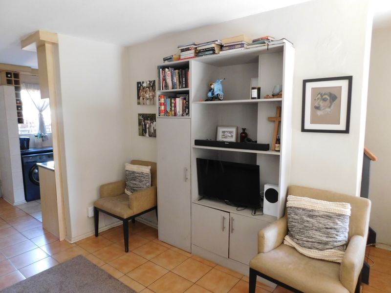 A living room area featuring a built-in shelving unit and tiled flooring, with an adjacent view into the kitchen space.