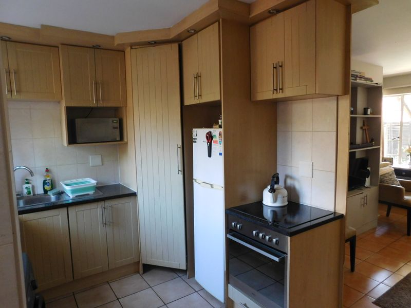 A functional kitchen featuring light wood cabinetry, tiled backsplash, built-in oven with hob, and tiled flooring, offering a practical layout for daily meal preparation.