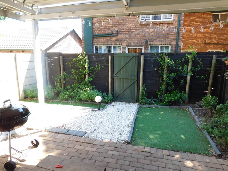A private rear patio area featuring brick paving, a small artificial lawn, gravel landscaping, and a secure timber gate leading to the exterior.