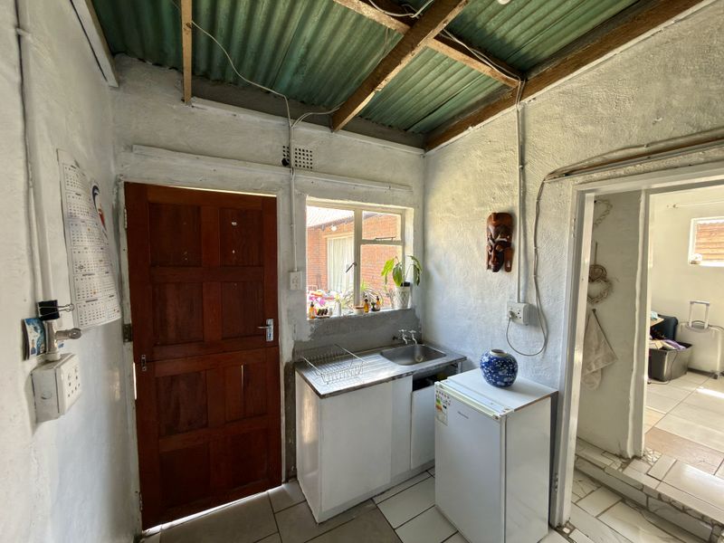 A compact scullery or utility area featuring a stainless steel sink, tiled flooring, and exposed corrugated roof structure.