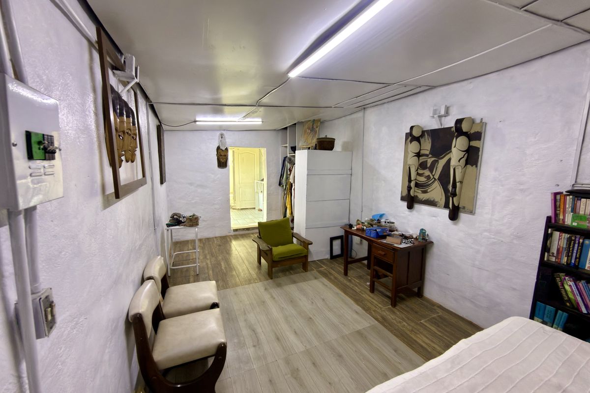 A living area featuring laminate flooring, white textured walls, and fluorescent lighting, providing a functional space with potential for modernization.