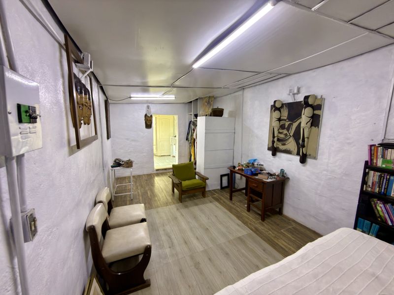 A living area featuring laminate flooring, white textured walls, and fluorescent lighting, providing a functional space with potential for modernization.