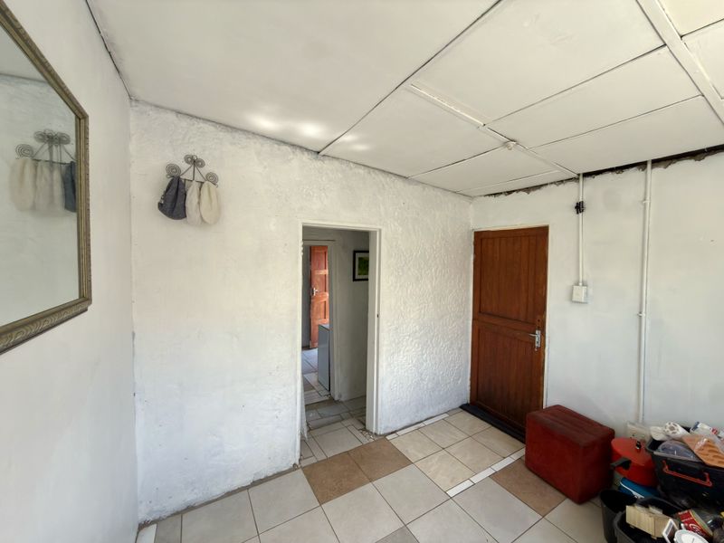 A simple entry area featuring tiled flooring, a timber door, and textured walls, providing a functional transition space within the cottage.