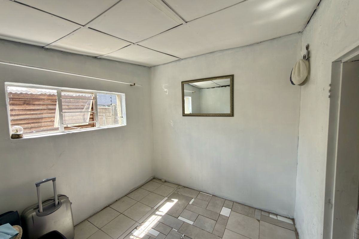 A small, empty bedroom featuring tiled flooring with some missing tiles, a drop ceiling, and an aluminium window frame.