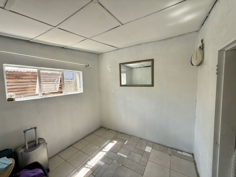 A small, empty bedroom featuring tiled flooring with some missing tiles, a drop ceiling, and an aluminium window frame.